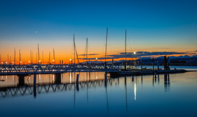 Beautiful sunset at the yacht harbor with pier. Summer sunset at the sea. Marina, port under dark blue sky at sunset
