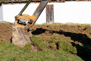 Fototapeta premium An bucket excavator in the village paves the way, digs soil and clears land.