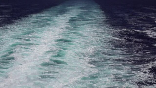 Waves from the back of a public ferry boat over the water's surface foam trace ship goes till the horizon as it travels across waving bright water