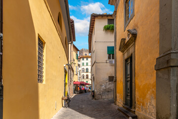 Fototapeta na wymiar A narrow street of homes, shops and cafes inside the walled medieval town of Lucca, Italy, with the Tower of Basilica San Frediano in view behind.