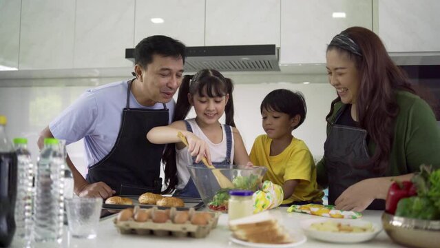 Asian families cook together on weekends. Happy families are helping each other make salads. Bake the bakery by looking at the recipes from the tablets in the kitchen. Family and teamwork concept