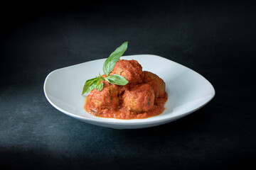 Italian meatballs seasoned with tomato sauce decorated with basil leaves