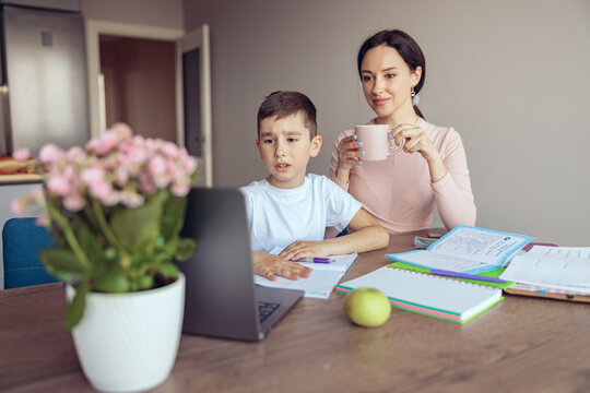 Confused Small Teen Boy Doing Homework Online At Laptop, Mother With Coffee Checking.