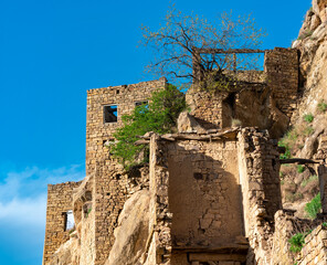 ruins of stone houses attached to the rock in the depopulated village of Gamsutl in Dagestan