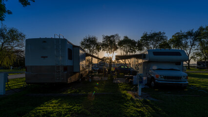 Sun rising early morning at campsites with Rv motorhomes and camper trailers parked door to door for companionship 
