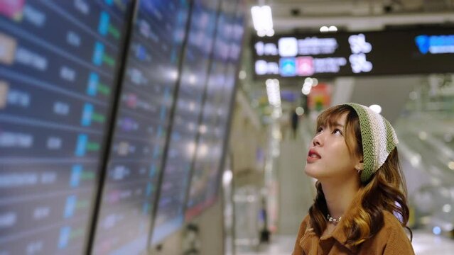 4K Young Asian woman passengers checking timetable flight schedule and walking to boarding gate in airport terminal. Attractive female traveler go to travel destination by airplane on holiday vacation