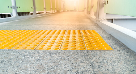Low view with flare.Yellow braille block with buttons raised above the surface. For warning to be cautious when pedestrians touch the embossed surface. Before going down the stair of overpass. - obrazy, fototapety, plakaty
