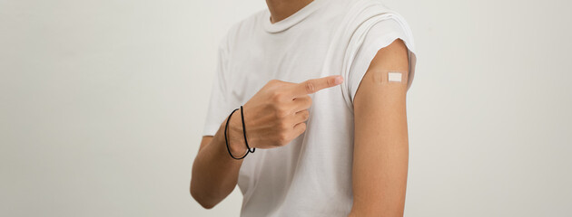 Happy Asian man showing his arm and bandage after they get a vaccine.