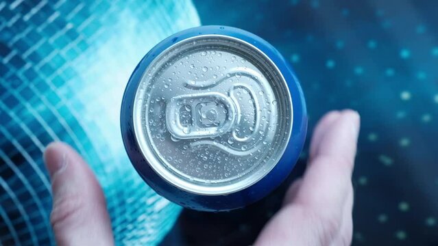 a man's hand takes a cold beer or a can of soda with drops of water. Drink drinks in aluminum cans with a latch. View from above. blue iridescent screen background
