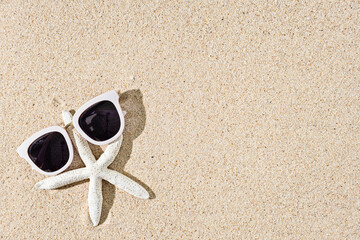 Fototapeta na wymiar Starfish and white sunglasses on natural sand background, copy space, top view