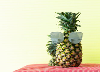 Pineapple with sunglasses on yellow background.