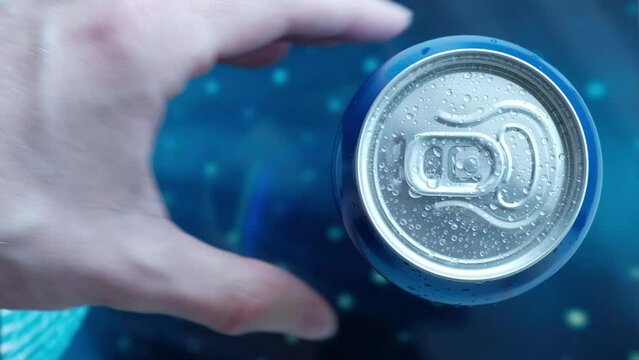 a man's hand takes a cold beer or a can of soda with drops of water. Drink drinks in aluminum cans with a latch. View from above. blue iridescent screen background
