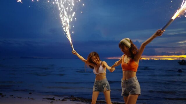 4K Young Asian woman having fun dancing and playing sparklers together on tropical island beach in summer night. Happy female friends enjoy outdoor lifestyle nightlife on holiday travel vacation trip