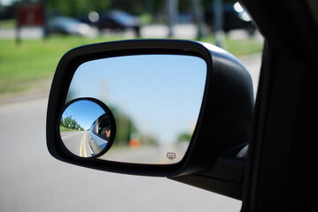 A round convex mirror (in focus) attached to a vehicle's side view mirror (rest of image, out of focus). The convex mirror provides a wider field of view .