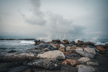 Beach on the Italian Riviera with sun, sea and stones in the sea water. Rough Sea and Foamy Waves on Shore at Mediterranean Coast in Sunrise