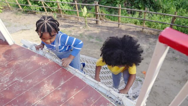 Happy Little African boy and girl friends climbing rope net together at outdoor playground in the park on summer vacation. Children kid enjoy outdoor activity playing and learning at school playground