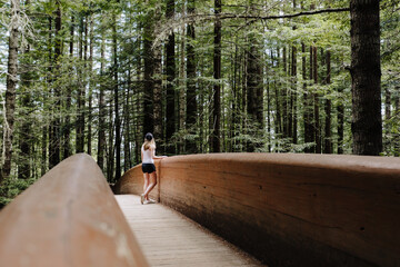 A young woman stands on the Lady Bird Johnson Grove Trail bridge in California Redwood National Park