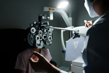 Ophthalmologist examining the eyes of an Asian girl in a clinic. They wear protective face masks.