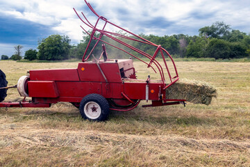 Old bale press, harvesting hay in the village for cattle, work of the press close-up.