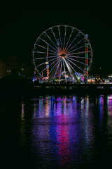 ferris wheel at night with reflection on water.