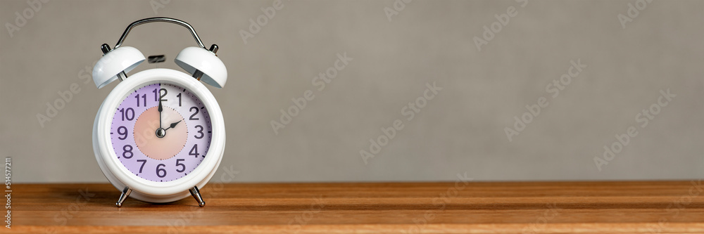 Poster two hours on the alarm. a white alarm clock stands on a wooden table. the clock hand points to 2 o'c