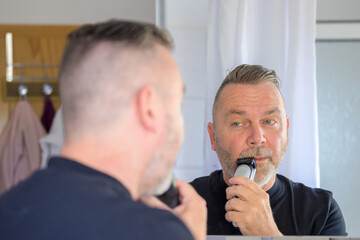 Middle-aged man trimming his moustache with clippers