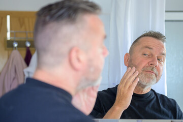 Senior man checking his facial skin in a mirror