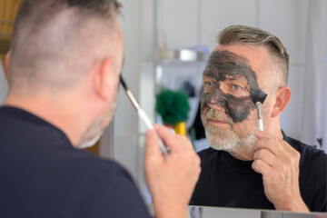 Senior man applying a face mask in a bathroom mirror