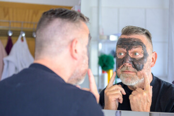 Fototapeta premium Middle-aged bearded man using a cosmetic face mask