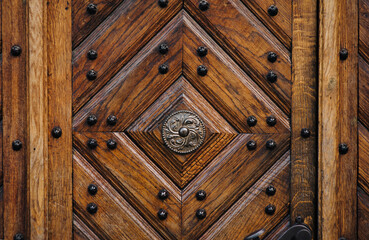 Old wooden dark brown door with diamond-shaped pattern in the rays of daylight. Vintage background