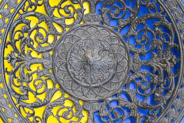 Part of openwork cast-iron plate on  yellow and blue backgrounds. Top view.