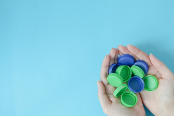 top view of hand holding plastic bottle caps with copy space on a blue background. recycling to conserve the environment.