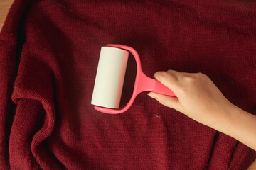 Woman using a sticky roller to clean sweater from dust and hair.