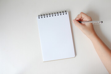 woman hand writing in empty notebook at the white desk. Flat lay top view.