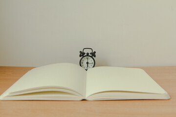 black alarm clock with notebook on wood background. Copy space.