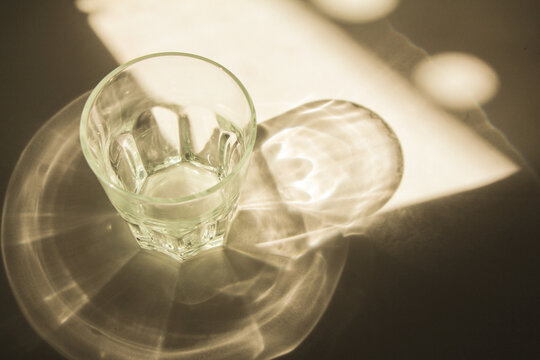 glass with sparkling sunlight shadow on the white background. Minimal luxury aesthetic concept. mock up and backdrop.
