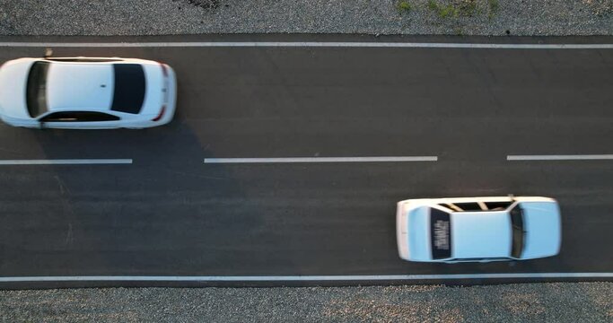 Two white cars drive along an asphalt road towards each other. Static video, Aerial view. The roadway from a height.