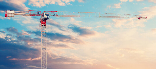 A red and white tower crane on a dramatic sky background with a space for text. High-quality photo for flyers, advertisements, banners