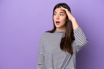 Young Brazilian woman isolated on purple background with surprise expression while looking side