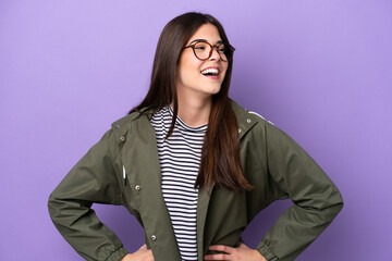 Young Brazilian woman isolated on purple background posing with arms at hip and smiling