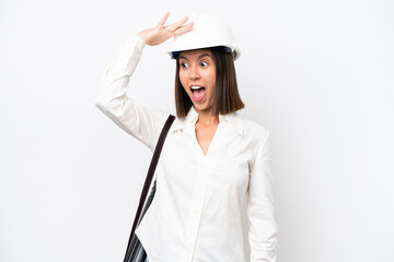 Young architect woman with helmet and holding blueprints isolated on white background doing surprise gesture while looking to the side