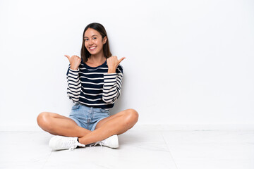 Young caucasian woman sitting on the floor isolated on white background with thumbs up gesture and smiling