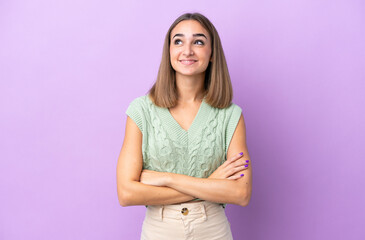 Fototapeta premium Young caucasian woman isolated on purple background looking up while smiling