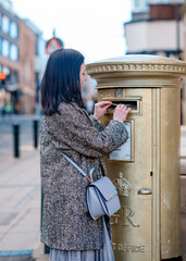 woman in grey coat posting letters in gold post box in England.  Olympic post box 