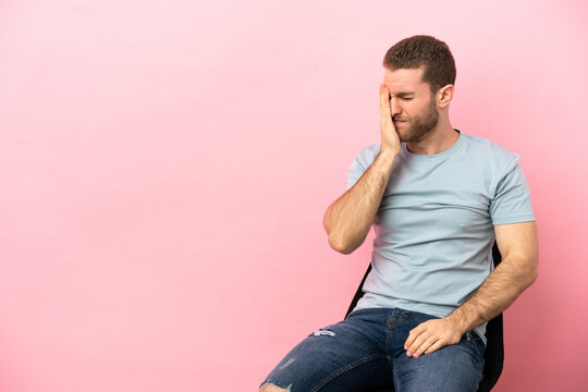 Young Man Sitting On A Chair Over Isolated Pink Background With Headache