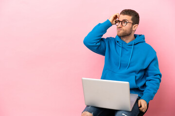 Young man sitting on a chair with laptop having doubts and with confuse face expression