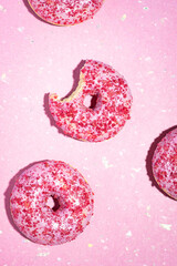 Donuts on pink background. Strawberry sprinkles on tasty, beautiful sugar glazed bitten dessert. Last bite. Girly, candy, pastry, sweet fast food, bakery, cafe minimal concept. Vertical, flat lay
