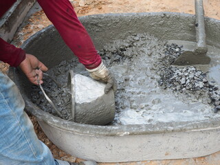 Workers use spade mixing wet cement in cement mixing basin. 
