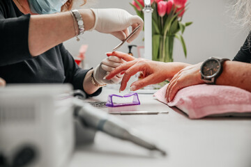 Manicurist master is covering painting client's nails shellac, hands closeup. Professional manicure in beauty salon. Hygiene and care for hands. Beauty industry concept. 