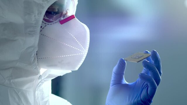 The concept of computer technology: An engineer in a sterile jumpsuit holds a computer microchip in his gloves and examines it. The concept of artificial intelligence